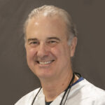 Here's an alt tag for the image: Smiling male doctor in scrubs.