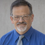 Here's an alt tag for the image: Headshot of man in blue shirt and tie.