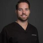 Man in black medical scrubs, smiling.